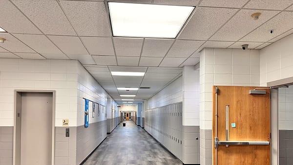 A bank of narrow metal lockers along a tiled corridor, one door slightly ajar, with light from a window at the far end