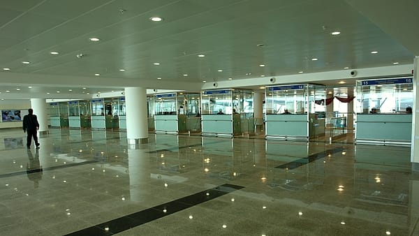 A passenger pulling a wheeled suitcase along an empty airport walkway lit by long ceiling panels at night.