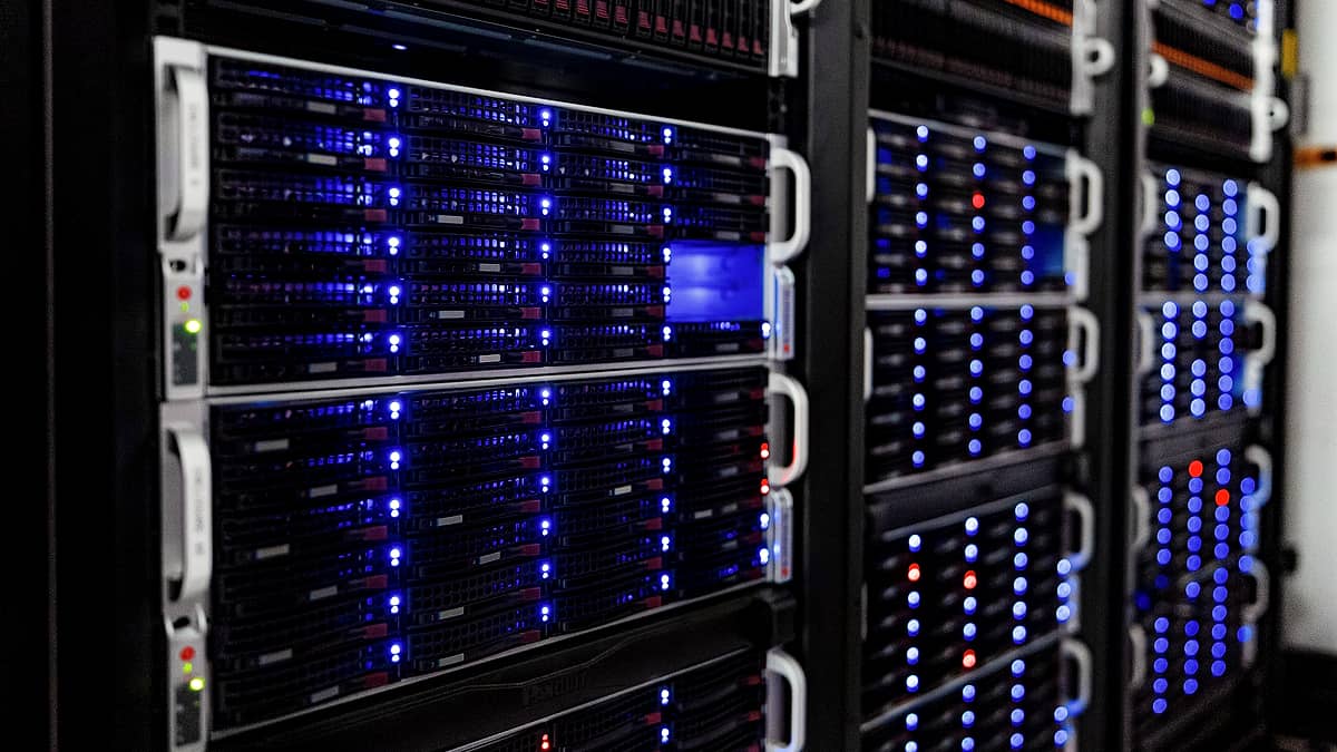 A server rack behind a glass door in a quiet windowless room, rows of small green status lights reflected in the panel